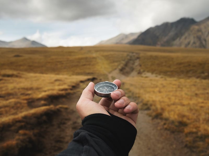An outstretched hand holding a magnetic compass with mountains in the background