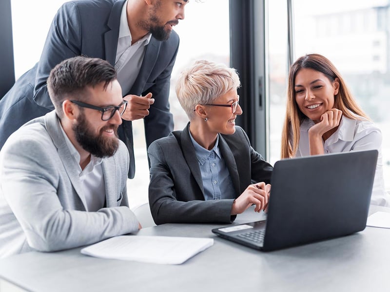 Four businesspeople gathered around a laptop in a meeting room