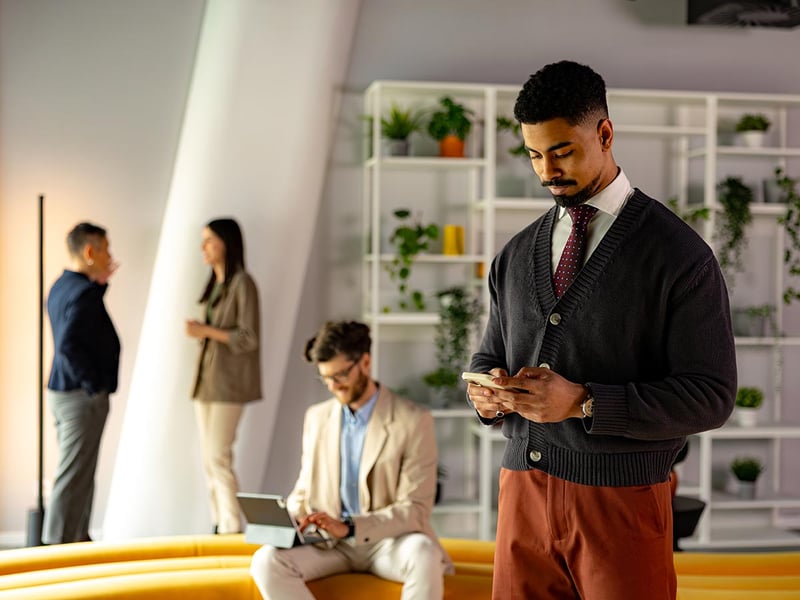Businessman using a smartphone in a modern office with colleagues working on tablets and talking in the background