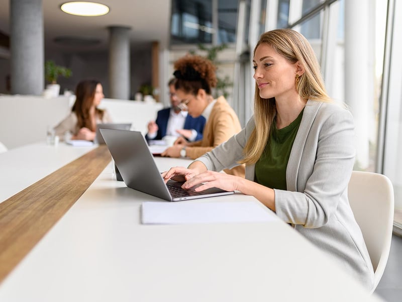 Woman analyzing a report on a laptop while working with colleagues in a meeting room