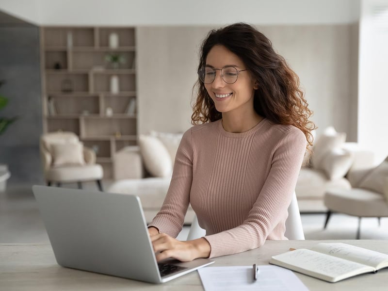 Smiling young woman in glasses working on a laptop at a desk in a home office 