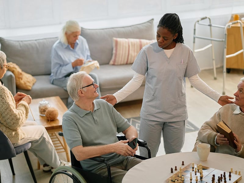 Female nurse talking with seniors sitting at a table with a chessboard on it at a senior living community