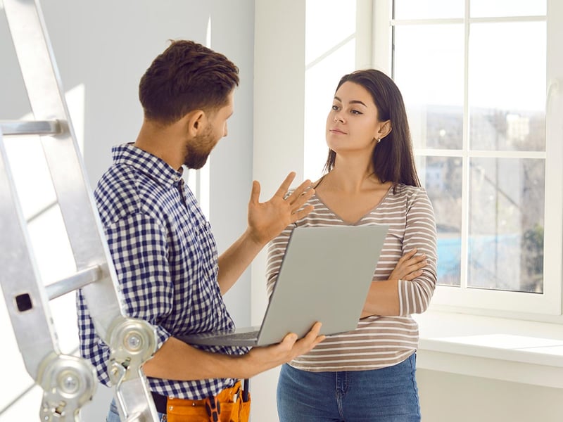 A repairman holding a laptop and talking to a woman at her home