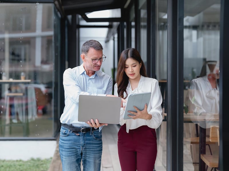 A senior businessman showing something on his laptop to a young businesswoman holding a tablet