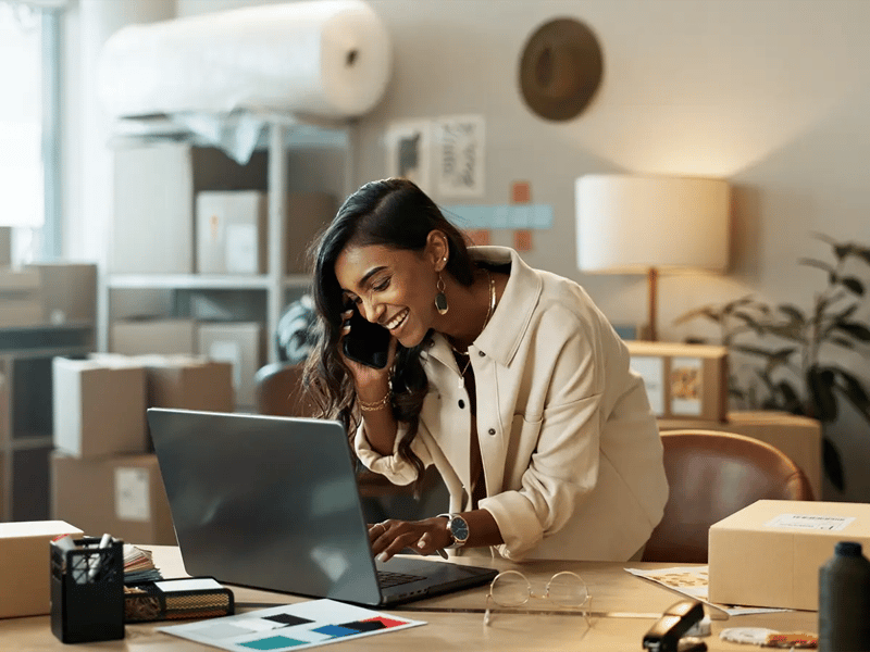 Smiling woman in an office on a phone call, using a laptop