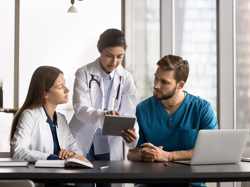 Female doctor mentor showing a male and female intern something on a tablet
