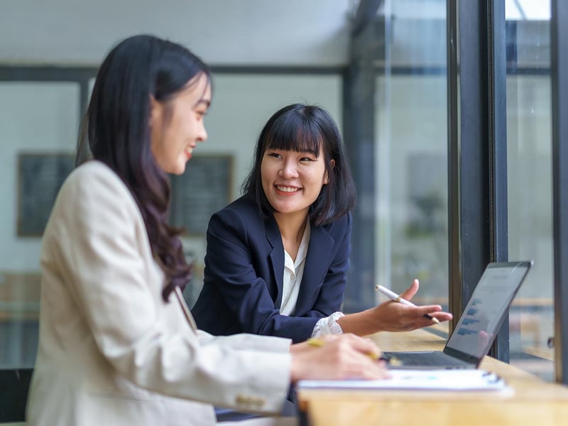 Two businesswomen discussing marketing strategy using laptop and taking notes in modern office
