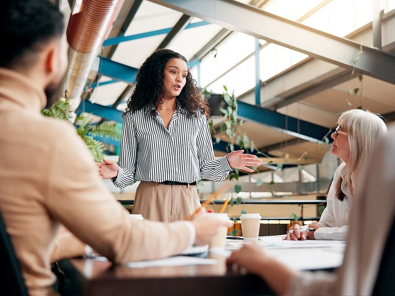 Young professional woman speaking to a group gathered around a conference room table